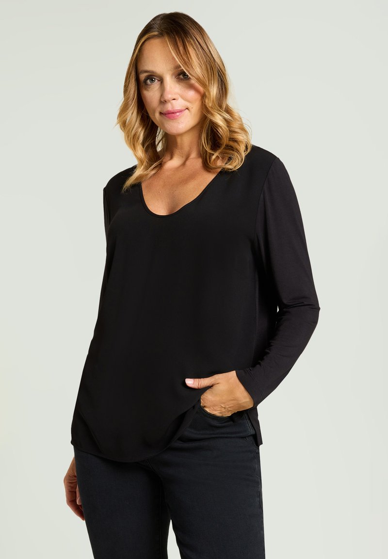 Schwarzes Langarm-Top mit Rundhalsausschnitt aus glattem Stoff, mit seitlichen Schlitzen und lockerer Passform, kombiniert mit dunkler Hose.