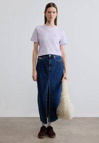 Λιλά μπλουζάκι με κοντά μανίκια, μακριά φούστα από μπλε τζιν με σκίσιμο μπροστά, καφέ αθλητικά παπούτσια και κρεμ υφασμάτινη τσάντα.