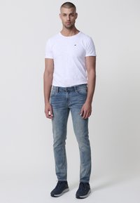 Fehér, rövid ujjú póló, slim-fit világoskék farmernadrág, és sötétkék sportcipő. Figyelemre méltó részletek közé tartozik egy kis logó a pólón.