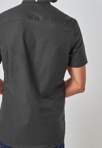 Camisa de manga corta en gris oscuro, hecha de una tela suave con cuello de botones y un diseño simple y limpio, que presenta un corte recto y costura trasera.