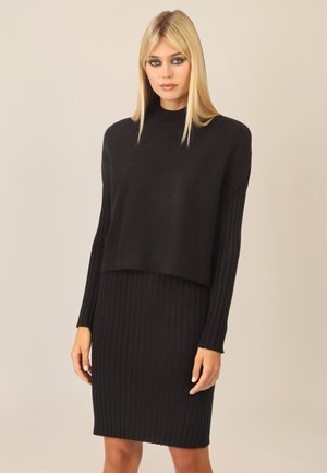 Schwarzes Strick-Zweiteiler-Set, bestehend aus einem kürzeren, gerippten Pullover mit langen Ärmeln und einem passenden gerippten Rock, beide aus einem weichen Material.