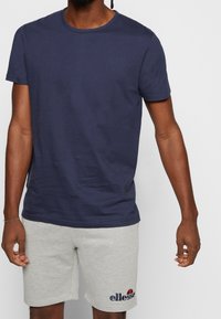 T-shirt en coton bleu marine avec un col rond et des manches courtes, assorti à un short gris avec un logo sur la jambe gauche.
