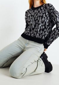 Svart och grå mönstrad tröja med ribbad halsringning och muddar; bärs med ljusblå jeans och svarta kängor med kraftig sula.