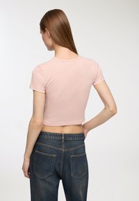 T-shirt a maniche corte di colore rosa chiaro, con scollatura rotonda e texture liscia, abbinata a jeans blu scuro con tasche posteriori.