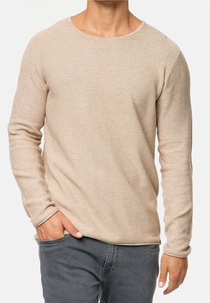 Beige neulepaita, jossa on pyöreä pääntie, pitkät hihat, teksturoitu kangas ja suora leikkaus, yhdistettynä harmaisiin farkkuihin.