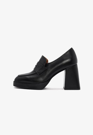 Des chaussures à talons hauts en cuir noir avec un bout arrondi, un détail de sangle à l'avant et un talon rectangulaire épais. Texture lisse et design épuré.