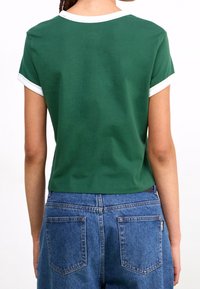 Grön kortärmad t-shirt med vit krage och ärmavslut, tillverkad av mjuk bomull, kombinerad med högmidjade denimjeans.