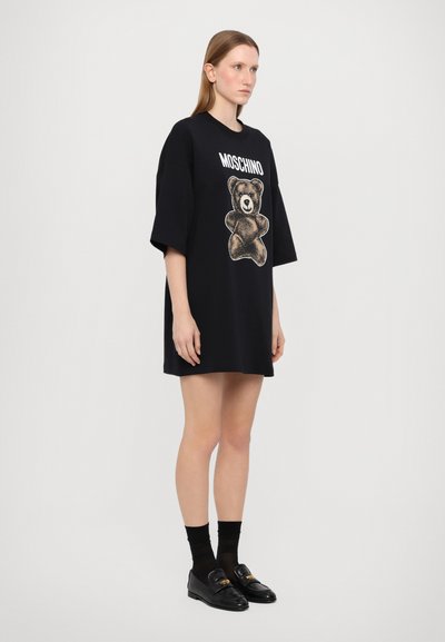 Svart oversized t-shirt klänning med en björngrafik och "Moschino"-text. Korta ärmar och rak nederkant. Mjuk bomullsmaterial.