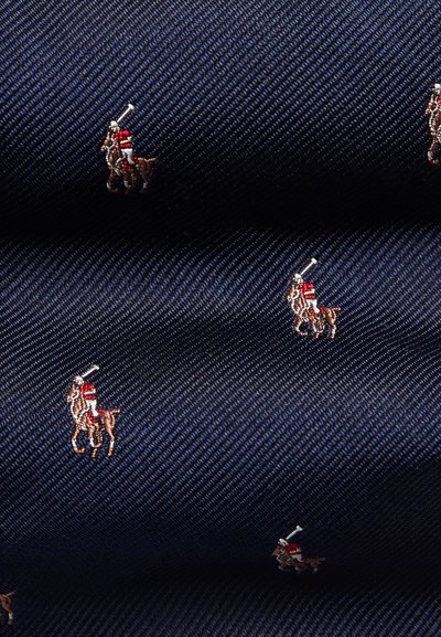 Marint tyg med diagonala ränder som pryds av små broderade polo-spelarmotiv i brunt och rött, vilka visar på intrikata detaljer och textur.