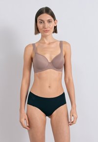 Rudas paminkštintas liemenėlė su plačiomis petnešėlėmis, lygiu paviršiumi ir apvaliais kaušeliais. Derinama su juodais be siūlių apatinius. Paprastas dizainas, be raštų.