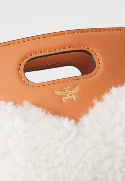 Tan læder skuldertaske med hvid fluffy tekstur, udstyret med en top-håndtag og et guld logo emblem. Rent design med minimalistiske accenter.