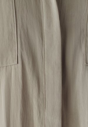 Tessuto beige con una superficie liscia, caratterizzato da cuciture verticali prominenti e due tasche quadrate su ciascun lato.