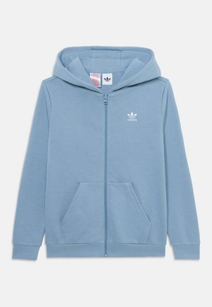 Felpa con zip di colore azzurro chiaro, realizzata in tessuto morbido. Presenta una tasca a marsupio, polsini a coste e un piccolo logo bianco di Adidas sul petto.