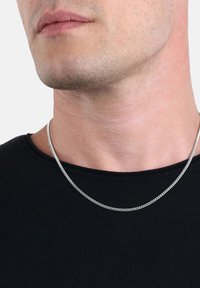 Zbliżenie dolnej części twarzy i szyi mężczyzny, który nosi cienki srebrny łańcuszek na czarnej koszuli.