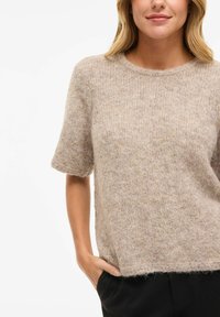 Beige strikket genser med korte ermer, rund hals, myk tekstur og en litt løs passform. Den nederste kanten har en subtil lodden avslutning.