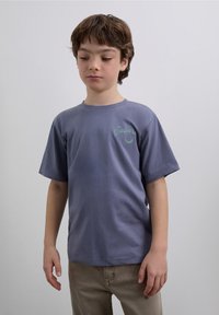 Lila T-Shirt mit kurzen Ärmeln aus Baumwolle, mit kleinem türkisfarbenem Logotext auf der linken Brust. Lockerer Schnitt mit rundem Ausschnitt.