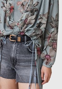 Blusa floreale in chiffon azzurro chiaro con maniche arricciate; abbinata a pantaloncini di jeans grigi a vita alta con orli sfrangiati e cintura nera.