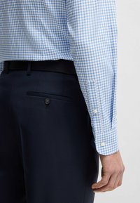 Jasnoniebieska koszula w biało-niebieskie kratki z zapiętymi mankietami, zestawiona z ciemnoniebieskimi spodniami z tylną kieszenią i zapięciem na guzik.