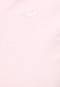 Tissu rose clair avec un petit logo de cheval brodé en fil rose légèrement plus foncé près du centre supérieur.