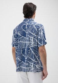 Camicia a maniche corte bianca con design a motivo foglia blu. Presenta un tessuto decorato e un colletto standard, mostrando una vestibilità comoda.