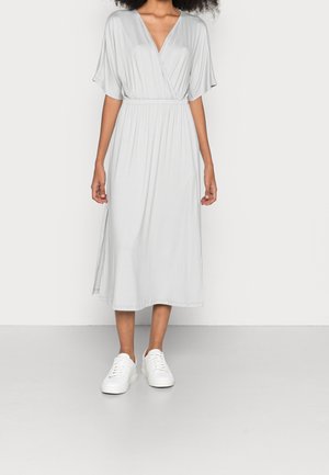 Vestido midi gris con un profundo escote en V y mangas murciélago. Fabricado con un tejido suave y fluido, con cintura elástica. Combinado con zapatillas blancas.