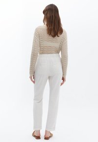 Lichtbeige gebreide trui met open weving, gecombineerd met crèmekleurige linnen broek met zijzakken. Tan instap schoenen.