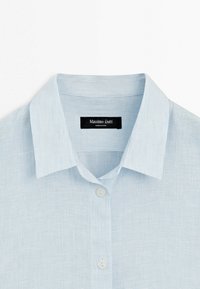 Hellblaues Hemd mit Kragen und feinen vertikalen Streifen, ausgestattet mit weißen Knöpfen und einem schwarzen "Massimo Dutti" Etikett innen am Kragen.