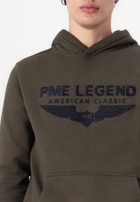 Ciemnooliwkowy hoodie wykonany z bawełny, z przednią kieszenią, posiada granatowy haftowany tekst oraz wzór skrzydeł na klatce piersiowej.