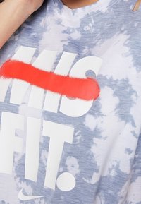 Camiseta de tie-dye azul claro con texto blanco en negrita que dice "MISFIT" tachado con pintura en spray roja. El logo de Nike es visible en la tela.