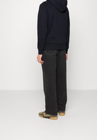 Svart hoodie med kängurufickor, i kombination med lösa mörka jeans och gröna och beige sneakers. Mjuk tyg och avslappnad passform.