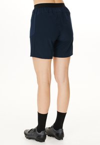 Marina atletiska shorts med en elastisk midja och sidofickor, med en slät yta och en snygg design. Svarta, texturerade skor med klackar.