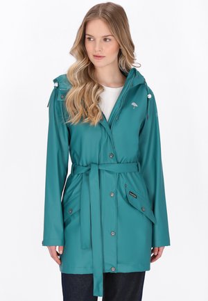 Donna che indossa un impermeabile verde acqua con cintura, cappuccio e tasche con pattina, in piedi davanti a uno sfondo bianco.