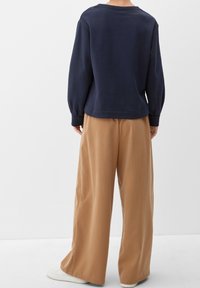 Marinblå sweatshirt med neddragna axlar, texturerat tyg och vida beige byxor i ett mjukt material, tillsammans med vita sneakers.