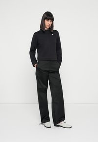 Sweatshirt noir court avec un col montant et des détails de couture à l'avant, associé à un pantalon cargo noir ample avec poches et poignets à cordon.