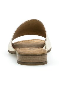 Ljusguld slide-sandal med en minimalistisk design, öppen bak och vadderad sula. Platt klack med texturerad sula för grepp.