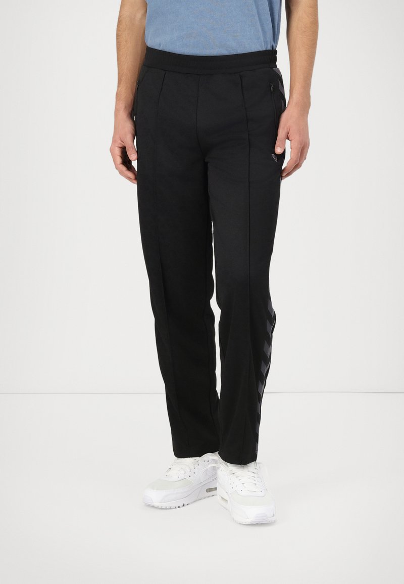 Black athletic pants with a smooth texture, featuring side zipper pockets and a striped pattern along the outer seam. Elastic waistband.