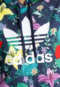 Sudadera de color navy con estampado floral y un gran logo de Adidas en blanco, que cuenta con capucha con cordones y flores de colores vibrantes a lo largo de la tela.