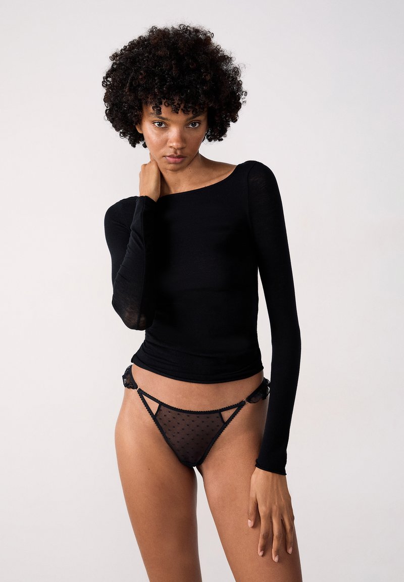 Maglia nera a maniche lunghe realizzata in un tessuto leggero con scollatura a barca, abbinata a perizoma trasparente nero a pois con dettagli in pizzo.