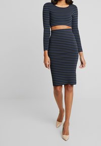 Striped two-piece set featuring a cropped long-sleeve top and a fitted midi skirt. Colors include navy and olive green. Smooth fabric texture.