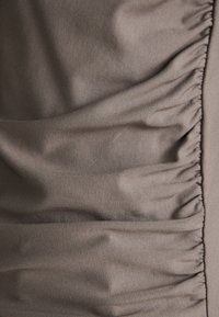 Tissu texturé dans un ton gris atténué, présentant des drapés doux et des accents froncés sur le côté, mettant en valeur une finition lisse.