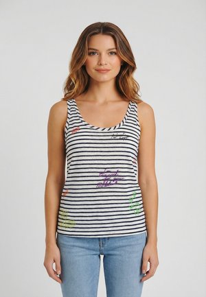 Joven con cabello hasta los hombros que lleva una blusa sin mangas a rayas blancas y azul marino con texto bordado en colores, combinada con jeans azul claro.