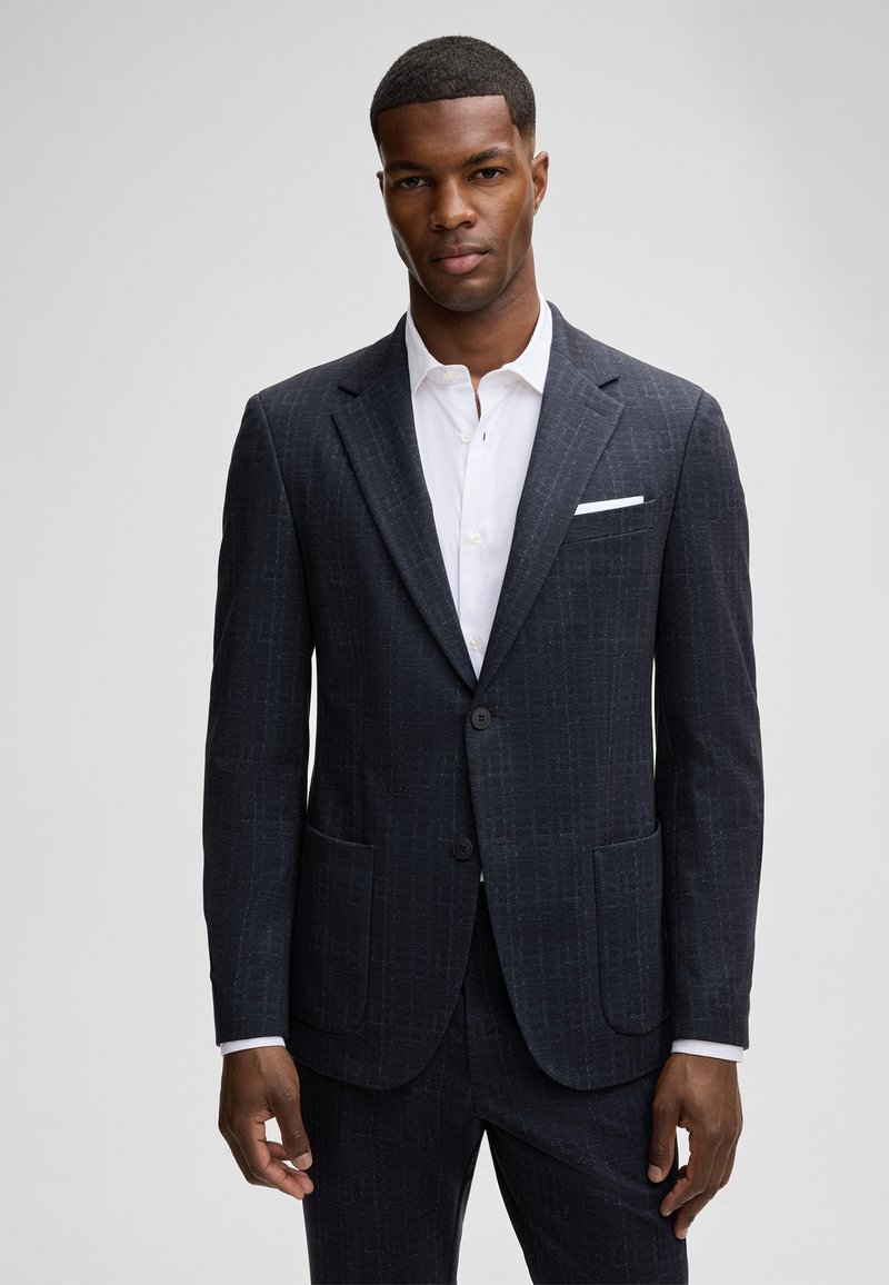 Donkerblauw pak met een subtiele geruite patroon, vervaardigd uit gestructureerde stof. Bevat een notched lapel, twee knopen en een borstzak.