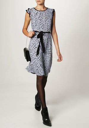 Robe à imprimé floral dans des tons de violet, avec des garnitures noires, des manches courtes à volants, une taille cintrée avec un ruban noir, silhouette en A, associée à des bottines noires.