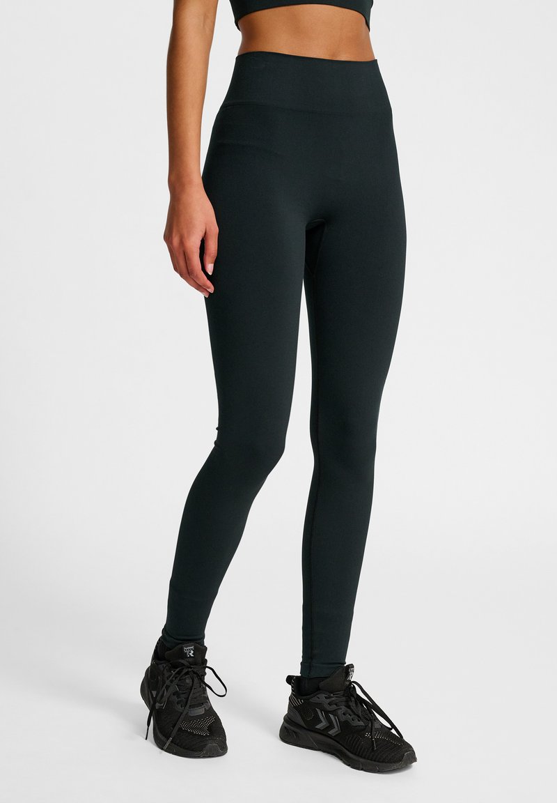 Hoge taille zwarte leggings gemaakt van een gladde, rekbare stof. Beschikt over een naadloos design en een aansluitende pasvorm. Draag het met zwarte sport schoenen.