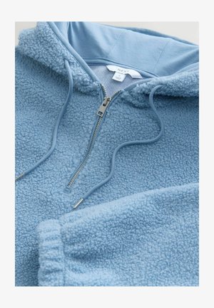 Sudadera de forro polar de color azul claro con media cremallera, tela texturizada, cordón ajustable y puños acanalados. Etiqueta visible en el cuello.