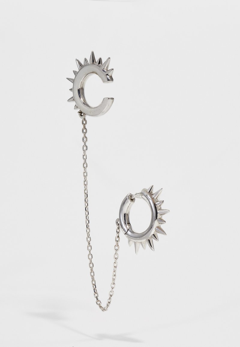 Sudraba auskari ar ādām līdzīgu dizainu; viens auskaru ir C formas, savienots ar ķēdi ar apaļu gredzenu, uz kura ir ādām.