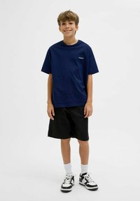T-shirt en coton bleu marine à manches courtes avec un petit logo, associé à un short noir et des baskets noir et blanc, portant des chaussettes blanches.