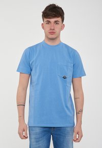 T-shirt in cotone blu chiaro con collo rotondo, maniche corte e una tasca sul petto con un patch a forma di triangolo nero.