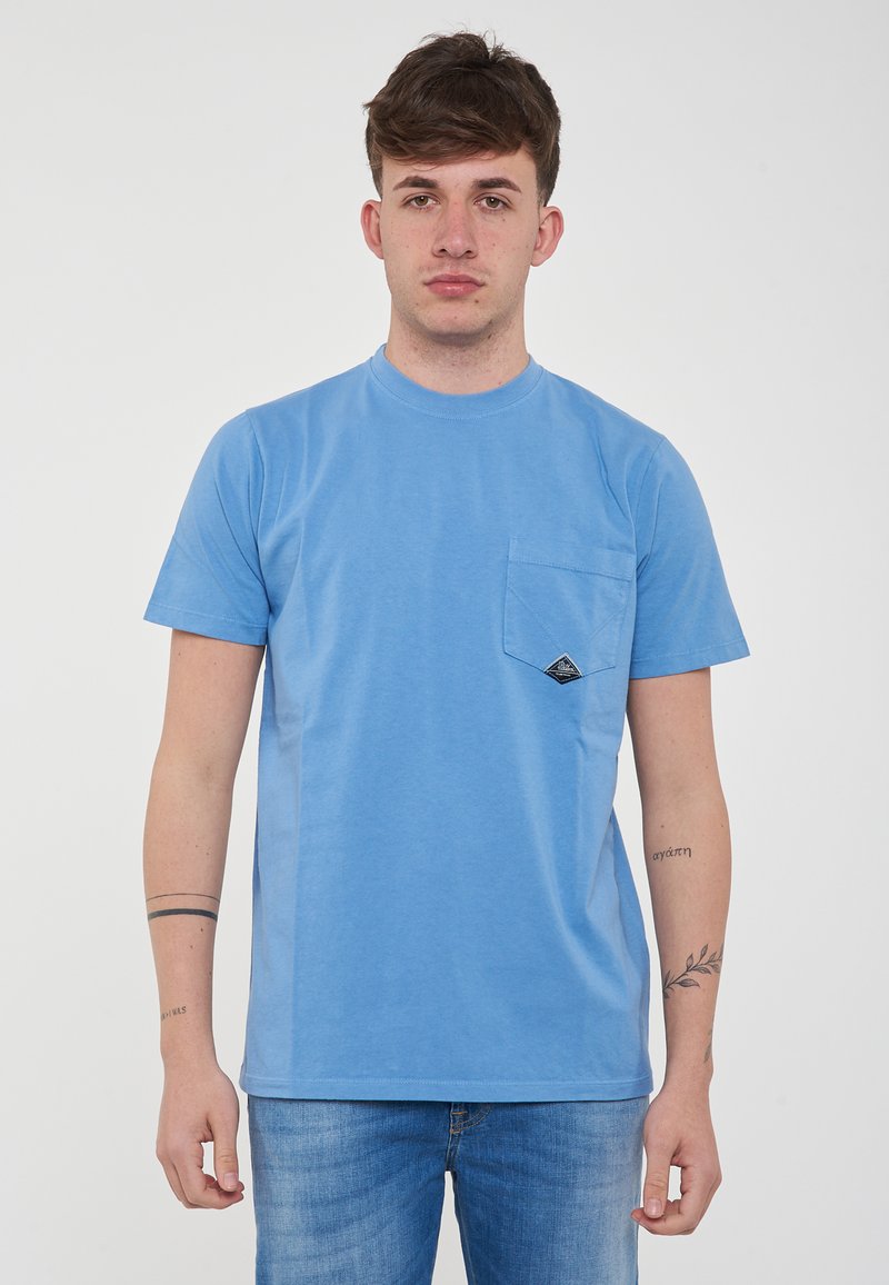 T-shirt in cotone blu chiaro con collo rotondo, maniche corte e una tasca sul petto con un patch a forma di triangolo nero.