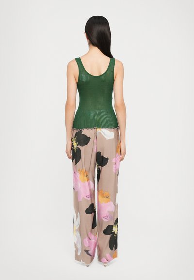 Grünes, geripptes Tanktop mit rundem Ausschnitt, kombiniert mit fließenden, weit geschnittenen Hosen, die große Blumenmuster in Pink, Schwarz und Weiß aufweisen.